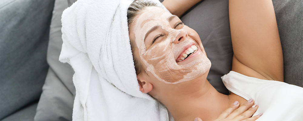 Mujer recostada sonríe mientras espera que una mascarilla facial haga efecto en su piel.
