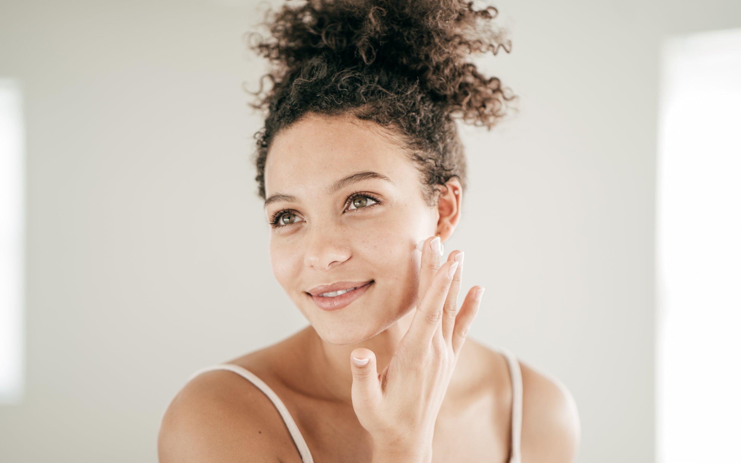 Mujer de piel morena con piel sensible aplica un protector solar facial adecuado a su tipo de piel, sin mostrar irritaciones.