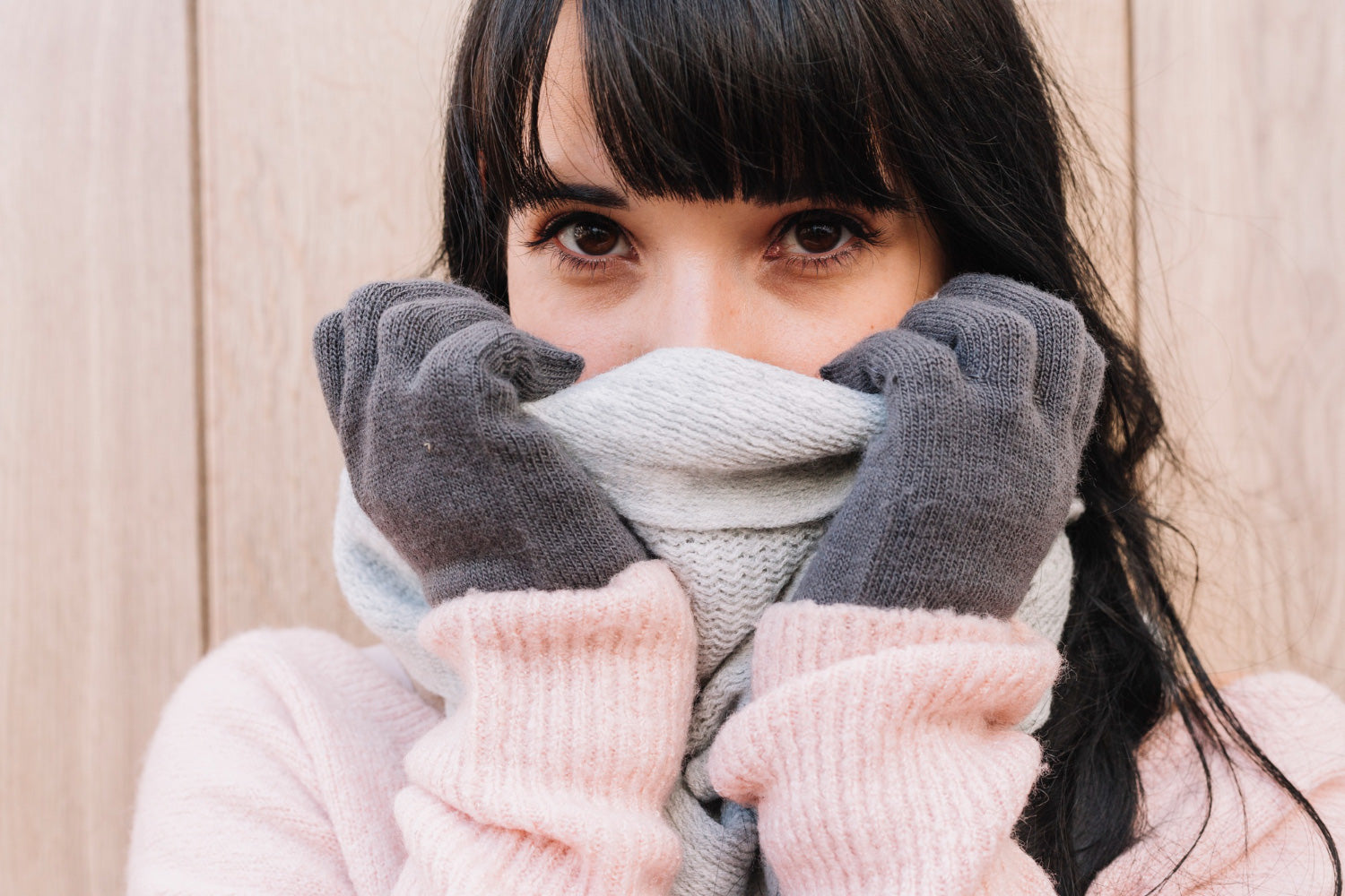 Mujer de cabello negro, y abrigada con ropa invernal, sostiene con las manos enguatadas una bufanda sobre su cara.