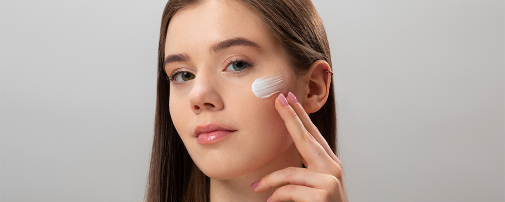 Rostro de mujer joven, con aplicación de protector solar para la cara. 