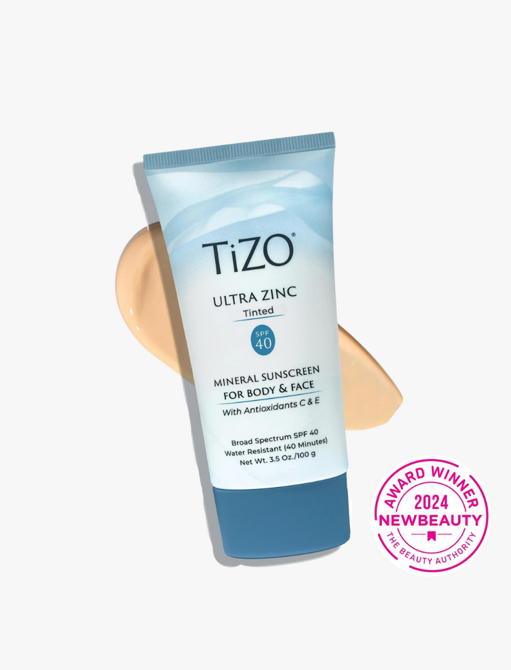 Envase azul degradado del protector solar Tizo Ultra Zinc SPF 40 con color, sobre fondo blanco, textura beige y sello NewBeauty 2024 en rosa