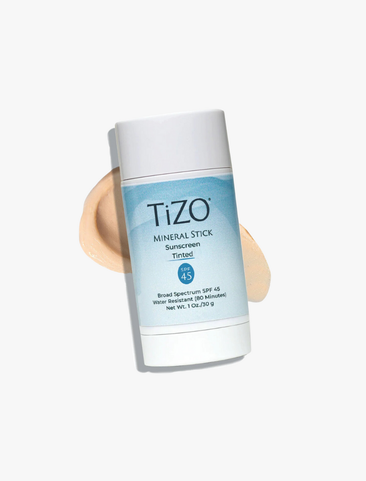 Envase del protector solar con color en barra TiZO Mineral Stick Tinted SPF 45 en tonos blancos y azules, al fondo textura con color piel y fondo blanco. 