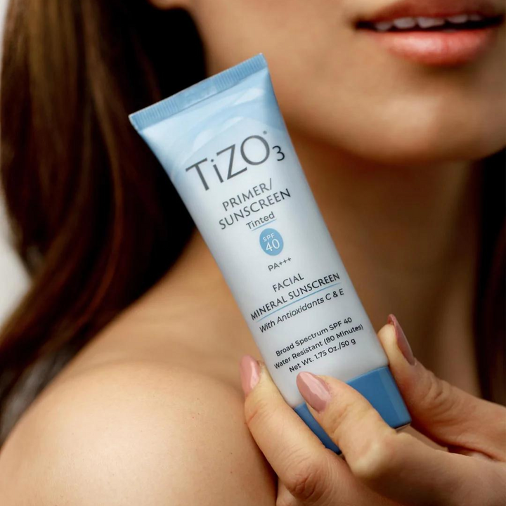 Mujer sosteniendo el envase del protector facial Tizo 3 con color y SPF 40, ideal para piel sensible.