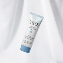  Envase del protector solar mineral Tizo 3 con color, un primer sunscreen con SPF 40 con acabado mate, suspendido sobre fondo blanco suave.